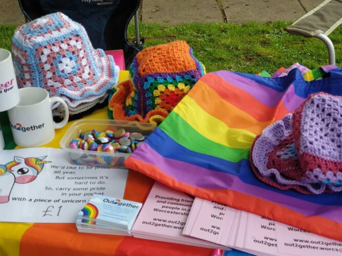 A table of rainbow gifts including hats and fabric, plus Out2gether leaflets